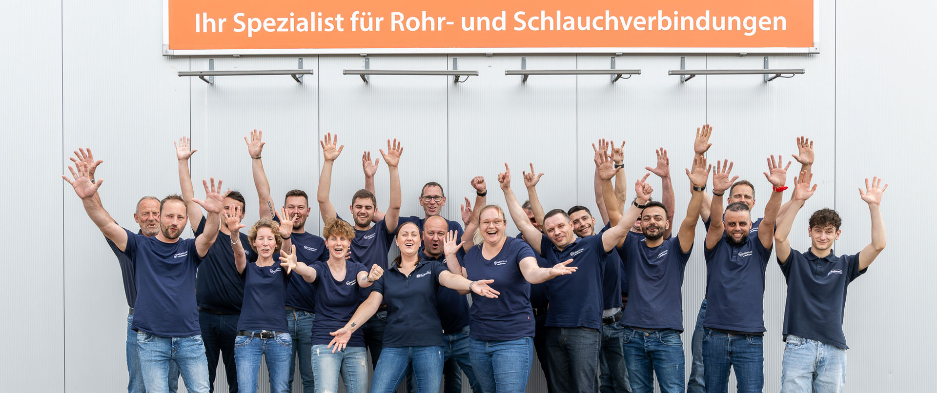 Mit uns sind Sie auf dem richtigen Weg! Mitarbeiter des Schellen-Shops stehen unter einem Banner mit dem Slogan "Ihr Spezialist für Rohr- und Schlauchverbindung"